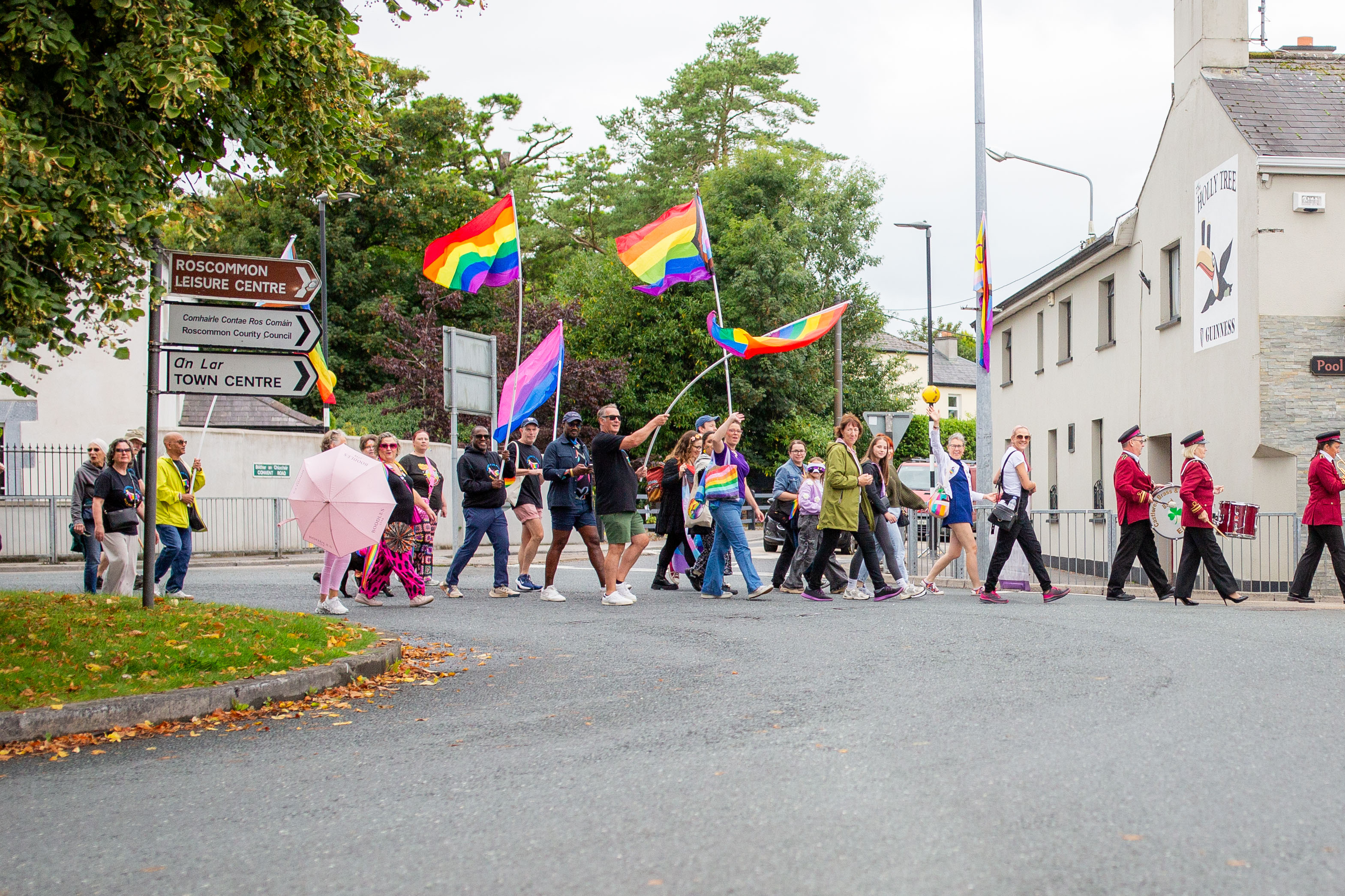 A vibrant Pride march with participants holding rainbow flags and banners, walking through a Roscommon street.